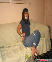 solo girl with painted toenails is hog tied & gagged on a sofa in her clothes