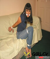 solo girl with painted toenails is hog tied & gagged on a sofa in her clothes