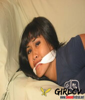 solo girl with painted toenails is hog tied & gagged on a sofa in her clothes