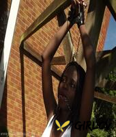 black girl is cleaved gagged and bound with her hands above her head in a yard